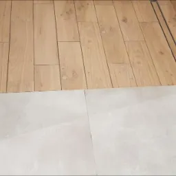 Wykończona podłoga w łazience z jasnymi płytkami imitującymi beton przechodzącymi w drewnopodobne panele z odpływem liniowym.