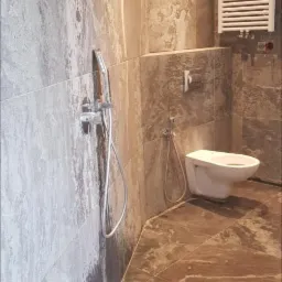 Wykończona łazienka z marmurowymi płytkami w odcieniach szarości i brązu, wisząca toaleta z bidetką, chromowana bateria prysznicowa i grzejnik drabinkowy.