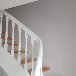 Best Color - Świeżo odnowiona klatka schodowa z drewnianymi schodami i białą balustradą, ściany pomalowane na jasny odcień bieli.