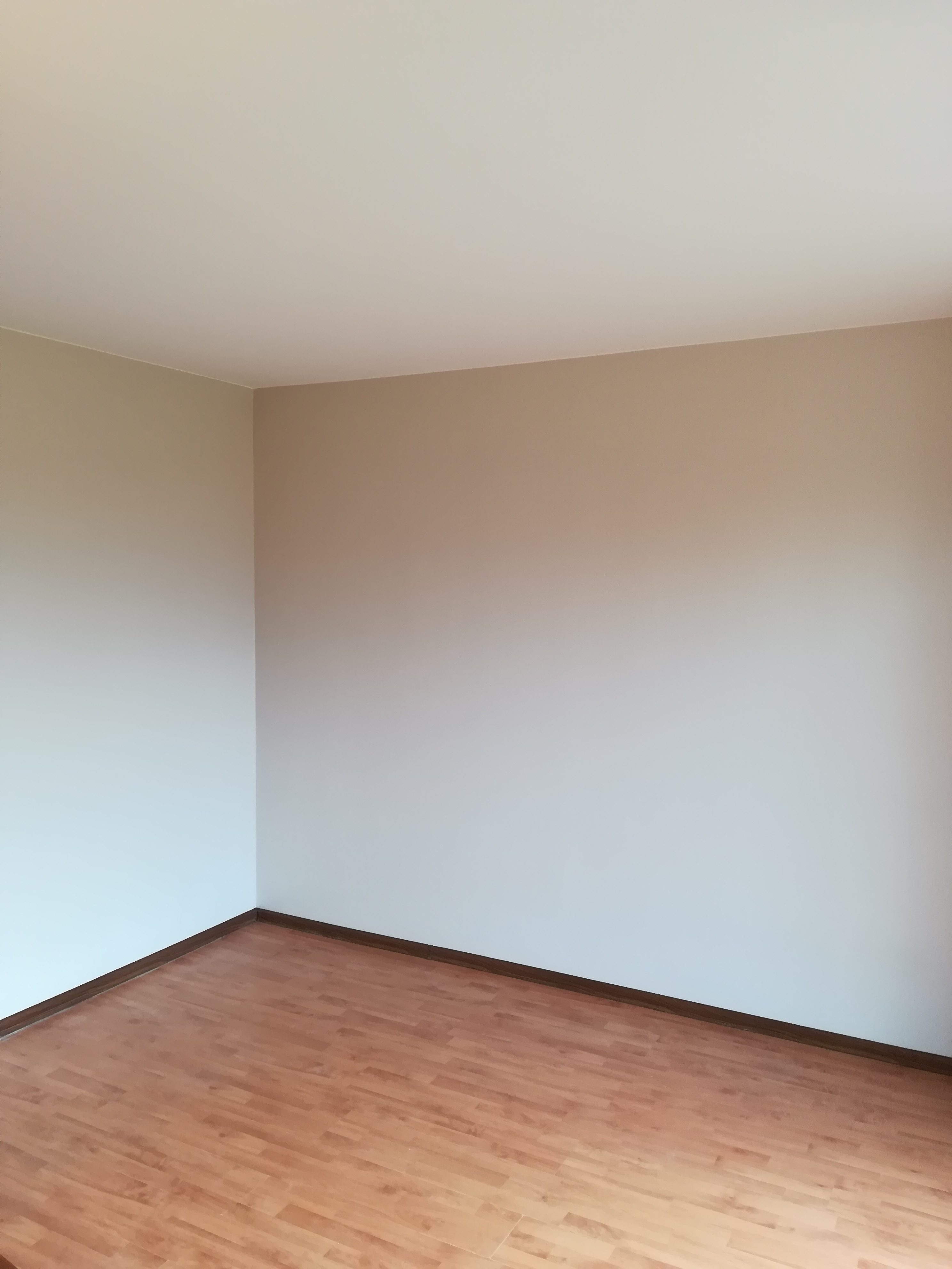 Pomalowane na beżowo ściany w pustym pokoju z panelami podłogowymi w odcieniach brązu, widok na róg pomieszczenia.