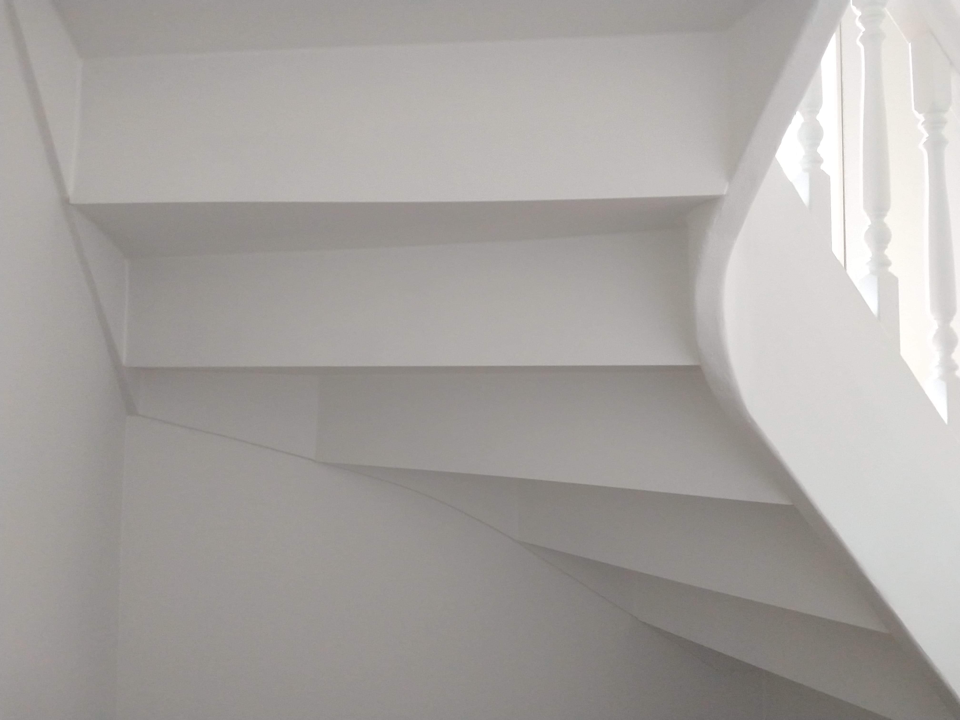 Biała, pomalowana klatka schodowa z drewnianą balustradą, widok z dołu, minimalistyczny design.