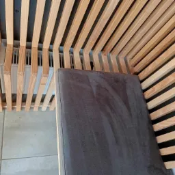 Nowoczesna antresola z drewnianymi listwami i szarą tapicerowaną powierzchnią, widok z góry na fragment konstrukcji z listew i siedzisko.