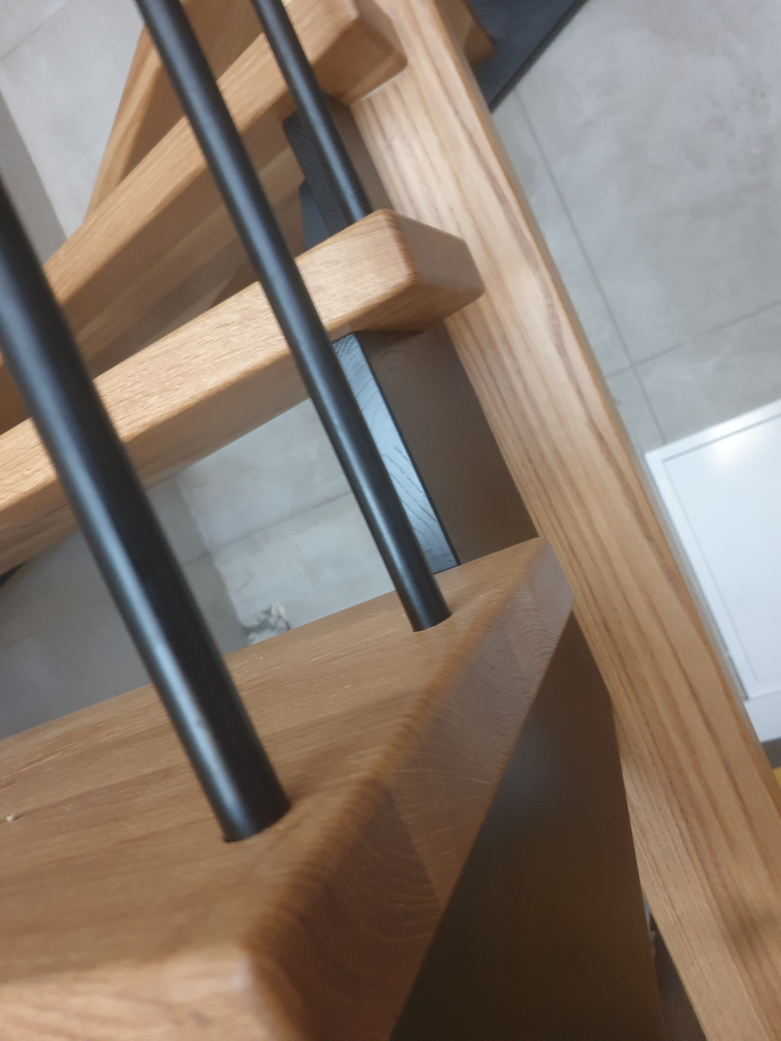 Fragment drewnianych schodów z czarnymi, metalowymi balustradami, widoczne z bliskiej perspektywy, ukazujące detale wykończenia i połączenia elementów.