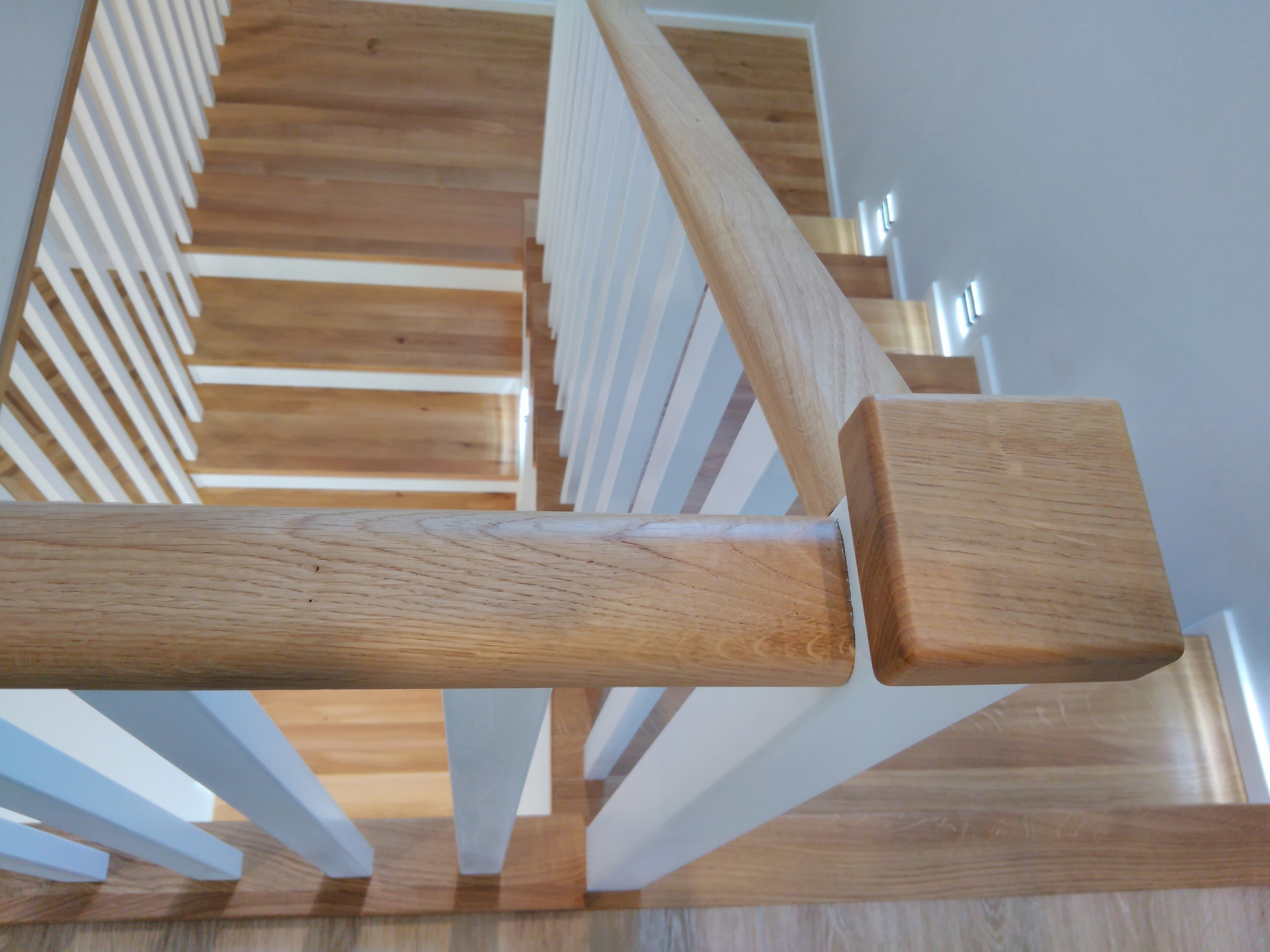 Jasne drewniane schody z białymi, pionowymi balustradami, widok z góry, kładący nacisk na detale drewna i minimalistyczny design.