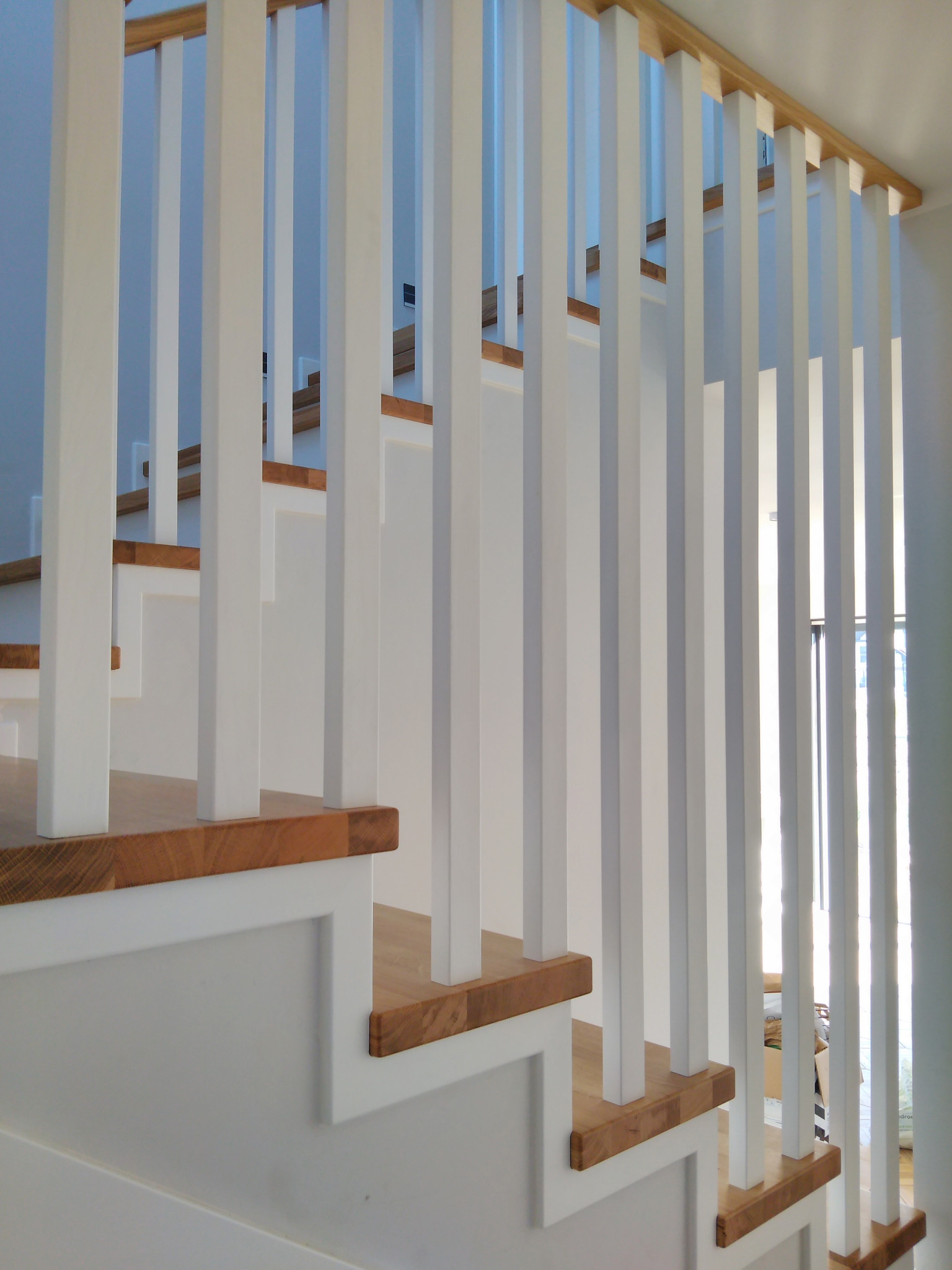 Nowoczesne schody z drewnianymi stopniami i białymi balustradami, widok z dołu, jasne wnętrze.