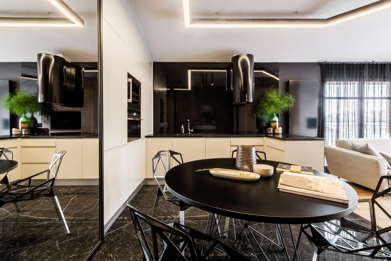 Nowoczesna kuchnia z czarną wyspą i marmurową podłogą, oświetlona ledowym światłem, z widocznym fragmentem salonu w tle.