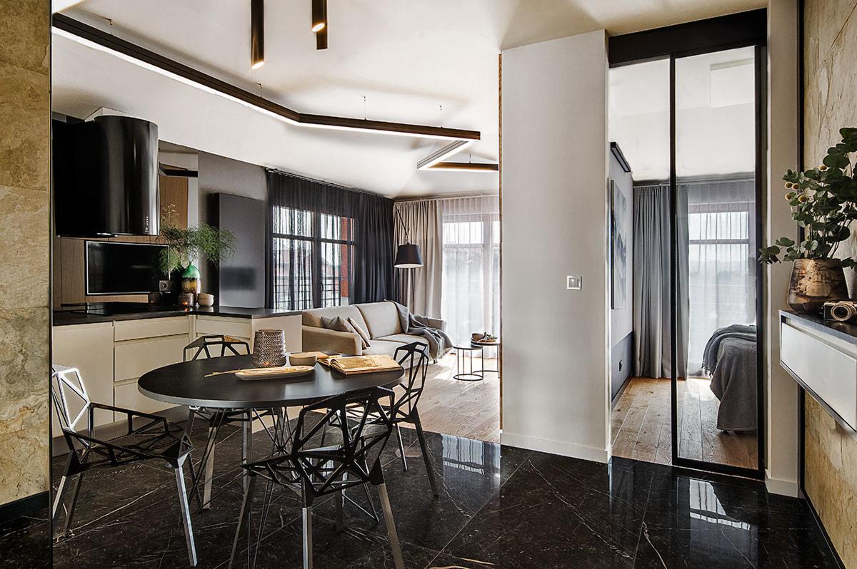 Nowoczesne wnętrze mieszkania z czarną marmurową podłogą, okrągłym stołem z czarnymi krzesłami, aneksem kuchennym i widokiem na salon przez otwarte przesuwne drzwi.