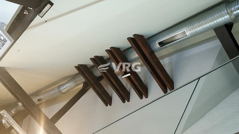 Widok na sufit z widocznymi elementami instalacji wentylacyjnej: metalowe rury wentylacyjne biegnące wzdłuż sufitu, ozdobione drewnianymi listwami w Muzeum Powstań Śląskich w Świętochłowicach.