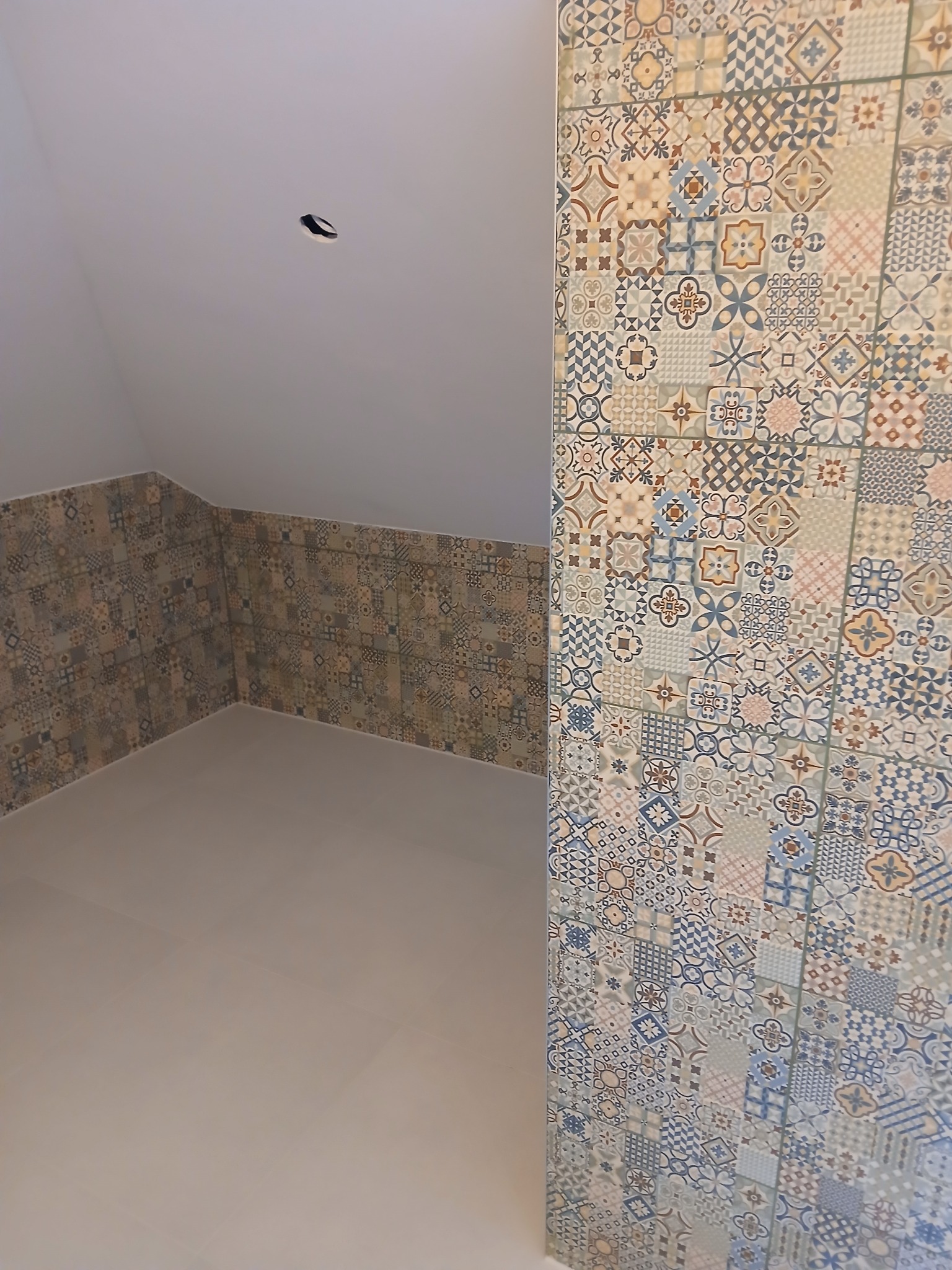 Ukończona łazienka na poddaszu z wzorzystymi płytkami na ścianach i podłodze. Płytki w odcieniach beżu, brązu i niebieskiego tworzą unikalny, dekoracyjny efekt.