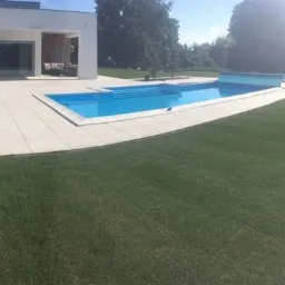 Nowoczesny ogród z basenem i równo ułożoną, ciemnozieloną powierzchnią trawnika, widok z boku.