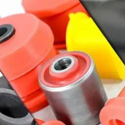 Kompozycja z obrobionych metalowych i poliuretanowych elementów zawieszenia samochodowego, z fragmentem pracy frezarki CNC w tle.