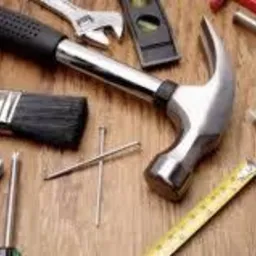 Zestaw narzędzi remontowych ułożonych na drewnianym blacie w Radwance: młotek, pędzel, poziomica, miarka, kombinerki, śrubokręt i inne akcesoria.