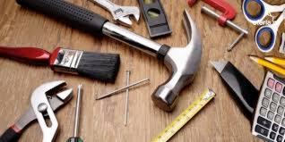 Zestaw narzędzi remontowych ułożonych na drewnianym blacie w Radwance: młotek, pędzel, poziomica, miarka, kombinerki, śrubokręt i inne akcesoria.