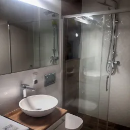 Nowoczesna łazienka z kabiną prysznicową typu walk-in, okrągłą umywalką nablatową na drewnianym blacie i pralką pod blatem.