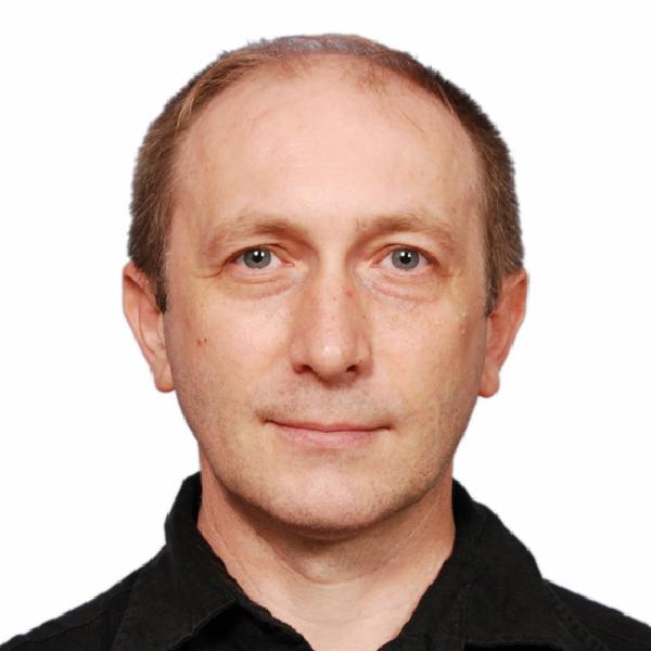 Portret mężczyzny w czarnej koszuli na białym tle, z delikatnym uśmiechem i niebieskimi oczami, prezentujący profesjonalizm tłumacza.