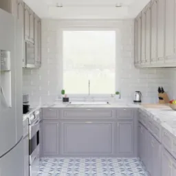 Wąska kuchnia w odcieniach szarości z wzorzystą biało-niebieską podłogą, widok na okno z zielenią na zewnątrz.