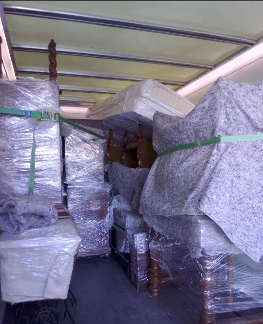 Mebel w folii i kocach, zabezpieczony pasami wewnątrz busa transportowego. Widok z wnętrza pojazdu podczas załadunku, przygotowanie do przeprowadzki.