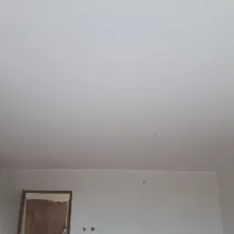 Wnętrze po malowaniu ścian i sufitu na biało, widoczne ślady po otworach na ścianie i futryna drzwi.