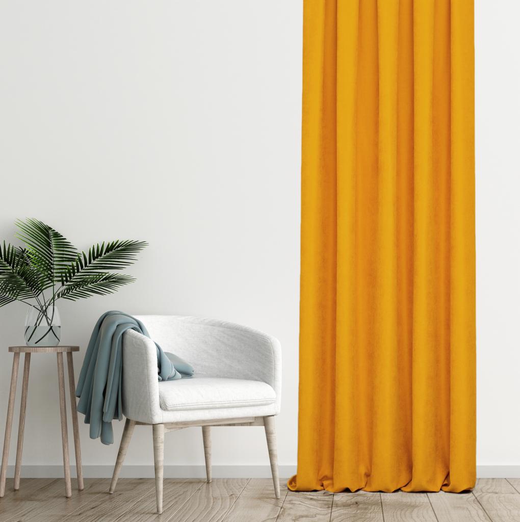 Jasny pokój z musztardową zasłoną, białym fotelem z narzuconym błękitnym pledem i stolikiem z rośliną w szklanym wazonie.