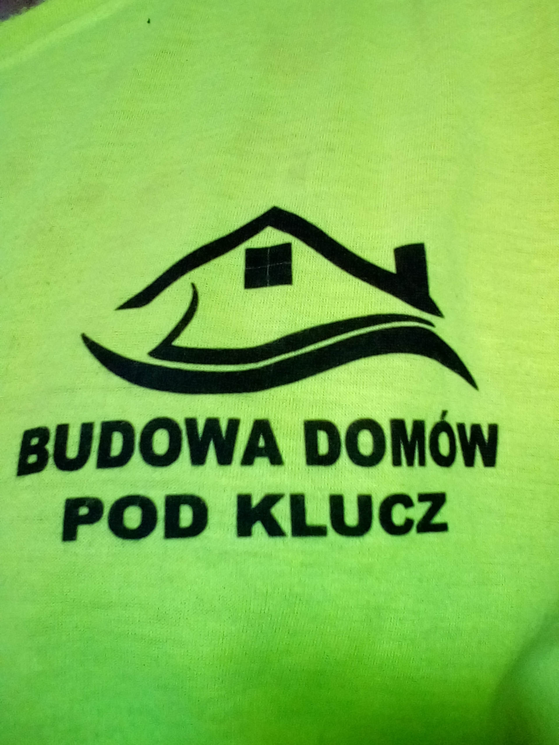 Neonowa koszulka z czarnym logo domu i napisem 'Budowa Domów Pod Klucz'.