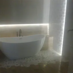 Nowoczesna wolnostojąca wanna w łazience z podświetleniem LED, białą cegiełką na ścianie i dekoracyjną mozaiką na podłodze.