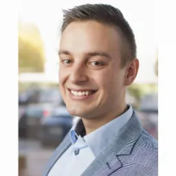 Uśmiechnięty mężczyzna w jasnej koszuli i marynarce w kratę na rozmytym tle miejskim. Profesjonalny portret.