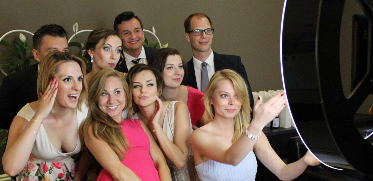 Grupa uśmiechniętych kobiet i mężczyzn pozuje do zdjęcia w fotobudce z okrągłym oświetleniem.