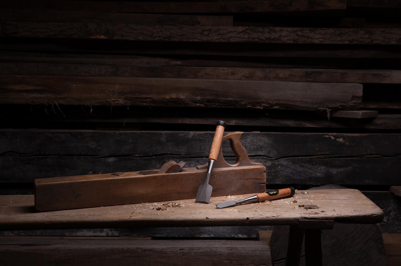 Stary drewniany strug i dwa dłuta leżące na blacie stołu warsztatowego z drewnianym tłem.