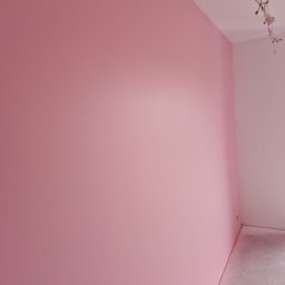 Krzysztof Krzyzowski. MACH-POL - Różowa ściana w nowo wykończonym pokoju, widoczne przewody elektryczne wystające z sufitu, szary betonowy podkład podłogowy.