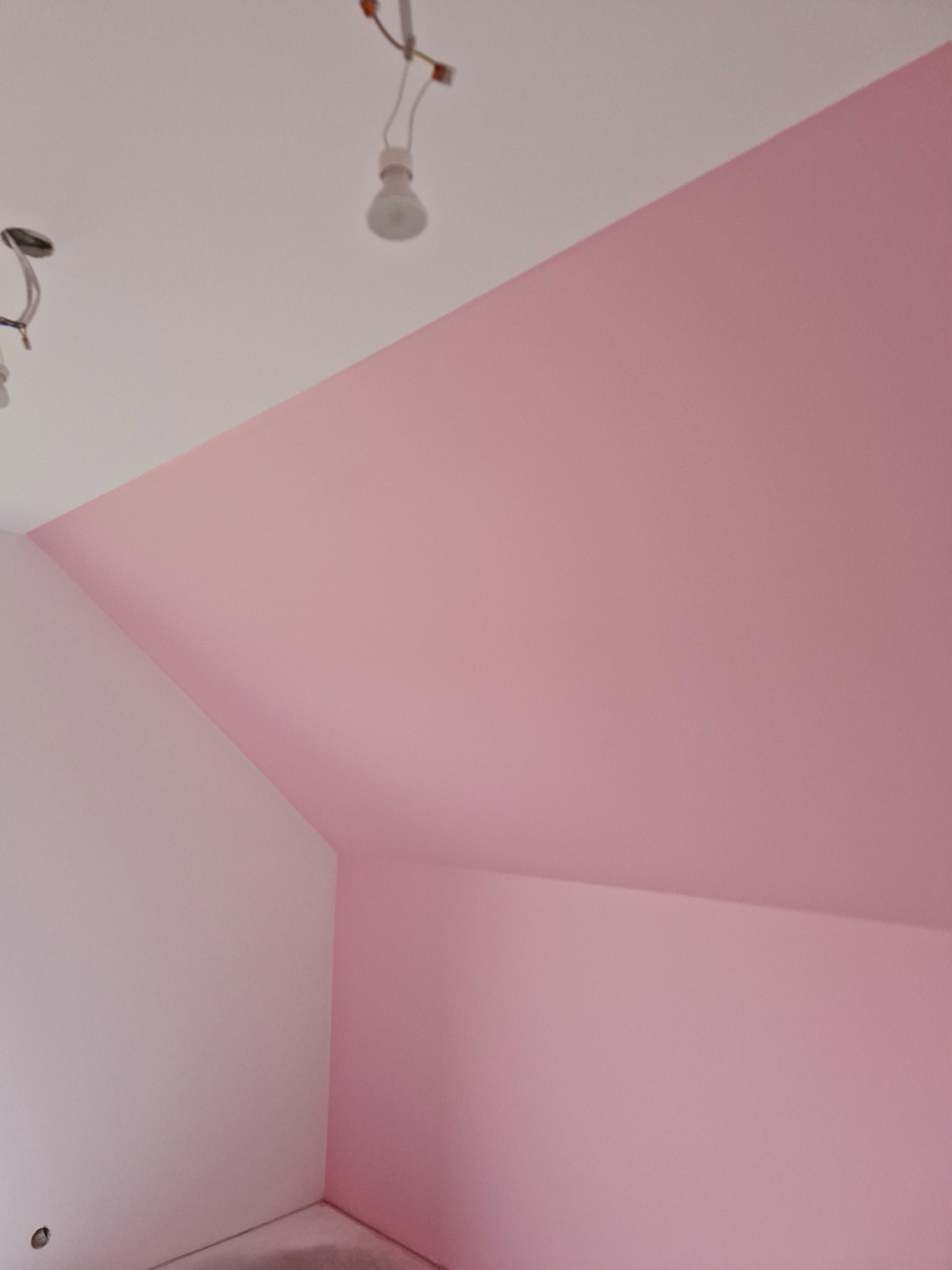 Pokój na poddaszu po częściowym pomalowaniu ścian na biało i różowo, widoczne niedokończone instalacje elektryczne na suficie.