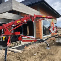 Czerwony mini-żuraw gąsienicowy z przyssawkami do szkła, podnosi okno podczas montażu w nowo budowanym domu z czerwonej cegły.