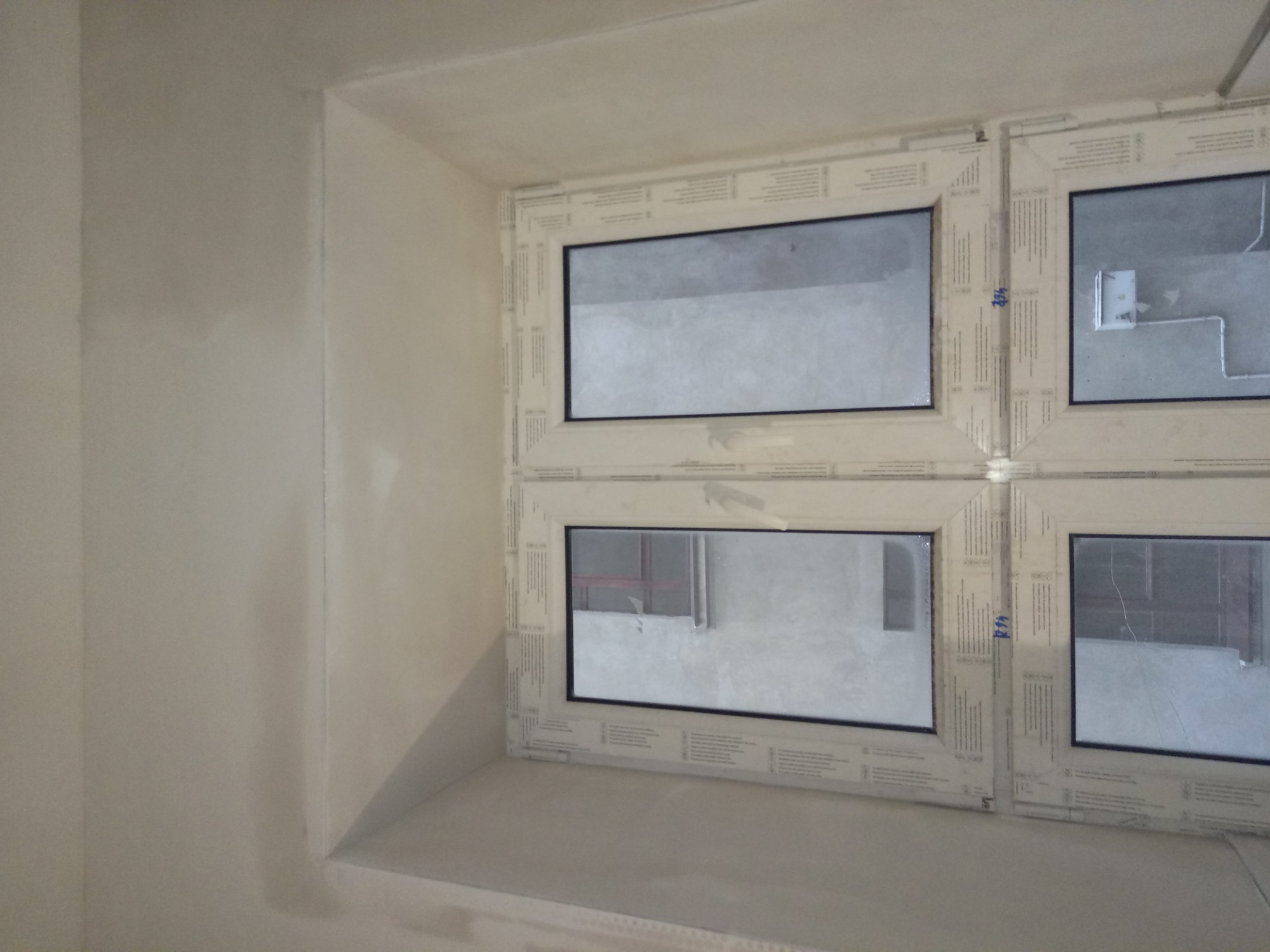 Świeżo oszpachlowana ściana i wnęka okienna z zamontowanymi oknami PCV przed malowaniem, widoczne ślady po łatach na ścianie.