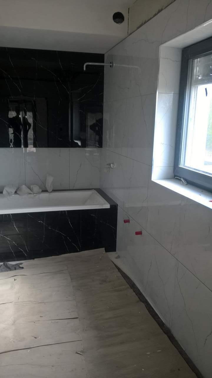 Łazienka w trakcie remontu: biało-czarne marmurowe płytki, częściowo zakryta podłoga, widoczne krzyżyki dystansowe na ścianie.
