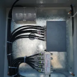 Wnętrze skrzynki z instalacją monitoringu: rozdzielacz sygnału, okablowanie i złączki.