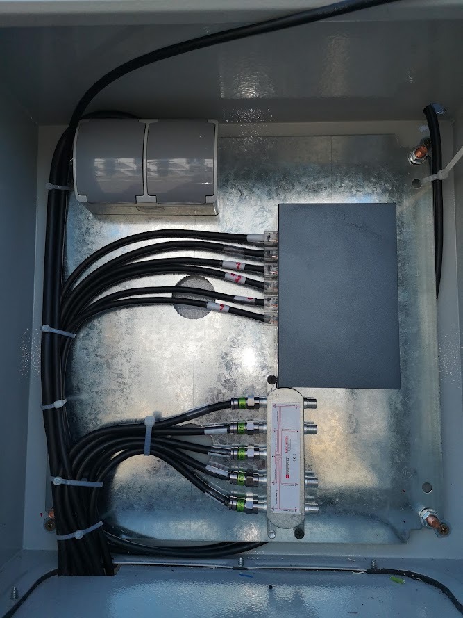 Wnętrze skrzynki z instalacją monitoringu: rozdzielacz sygnału, okablowanie i złączki.