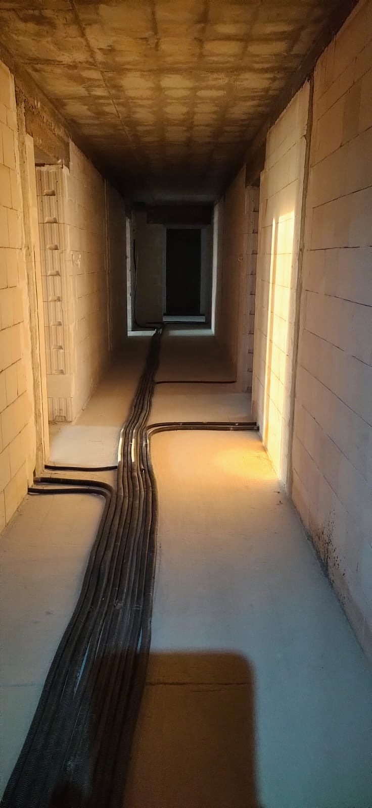 Korytarz w stanie surowym z ułożonymi kablami elektrycznymi w peszlach, widoczne ściany z bloczków i surowy betonowy strop