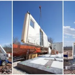 Montaż modułowej konstrukcji domu: dźwig podnosi prefabrykowany element ściany z oknem na placu budowy.