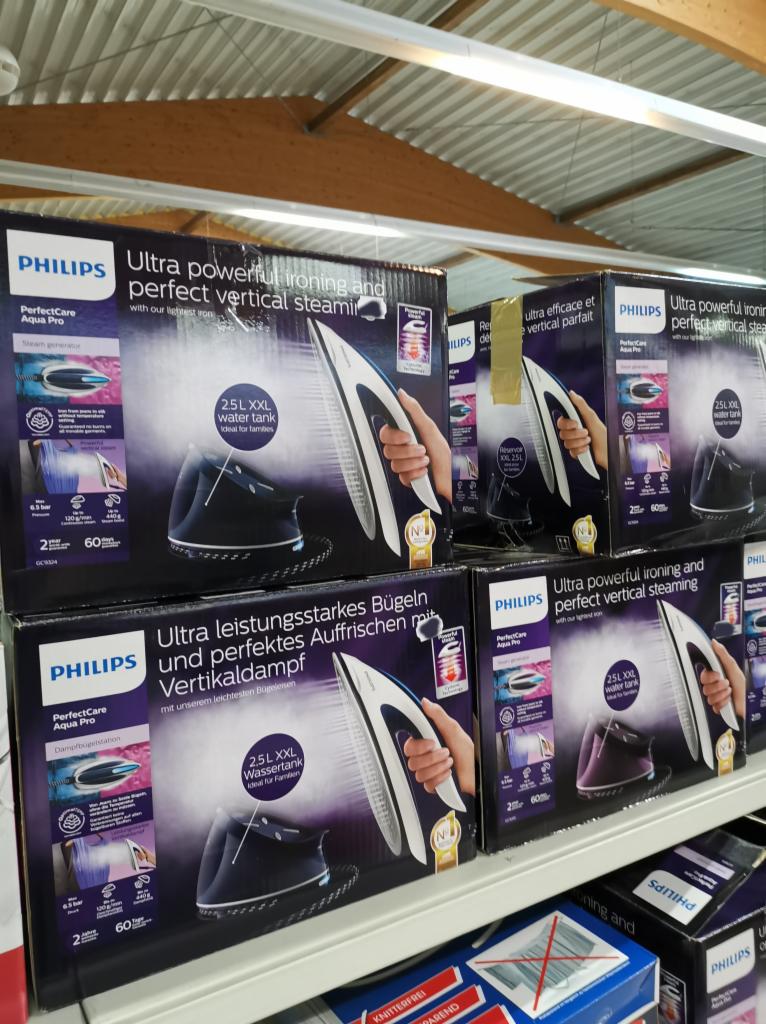 Półka sklepowa z pudełkami parowych żelazek Philips PerfectCare Aqua Pro z informacją o mocy, generatorze pary i pojemności zbiornika na wodę XXL 2.5L, widoczne w różnych językach.