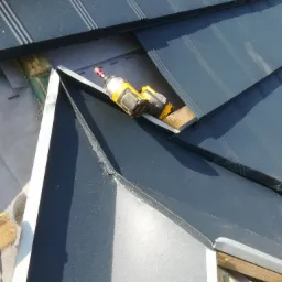 Montaż ciemnoszarej blachy na dachu z użyciem wkrętarki akumulatorowej, widoczne elementy konstrukcji drewnianej i membrana dachowa.