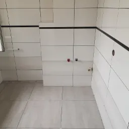 Świeżo wykafelkowana łazienka z szarymi płytkami podłogowymi i białymi płytkami ściennymi z czarnymi akcentami, widoczne wyprowadzenia instalacji wodnej.