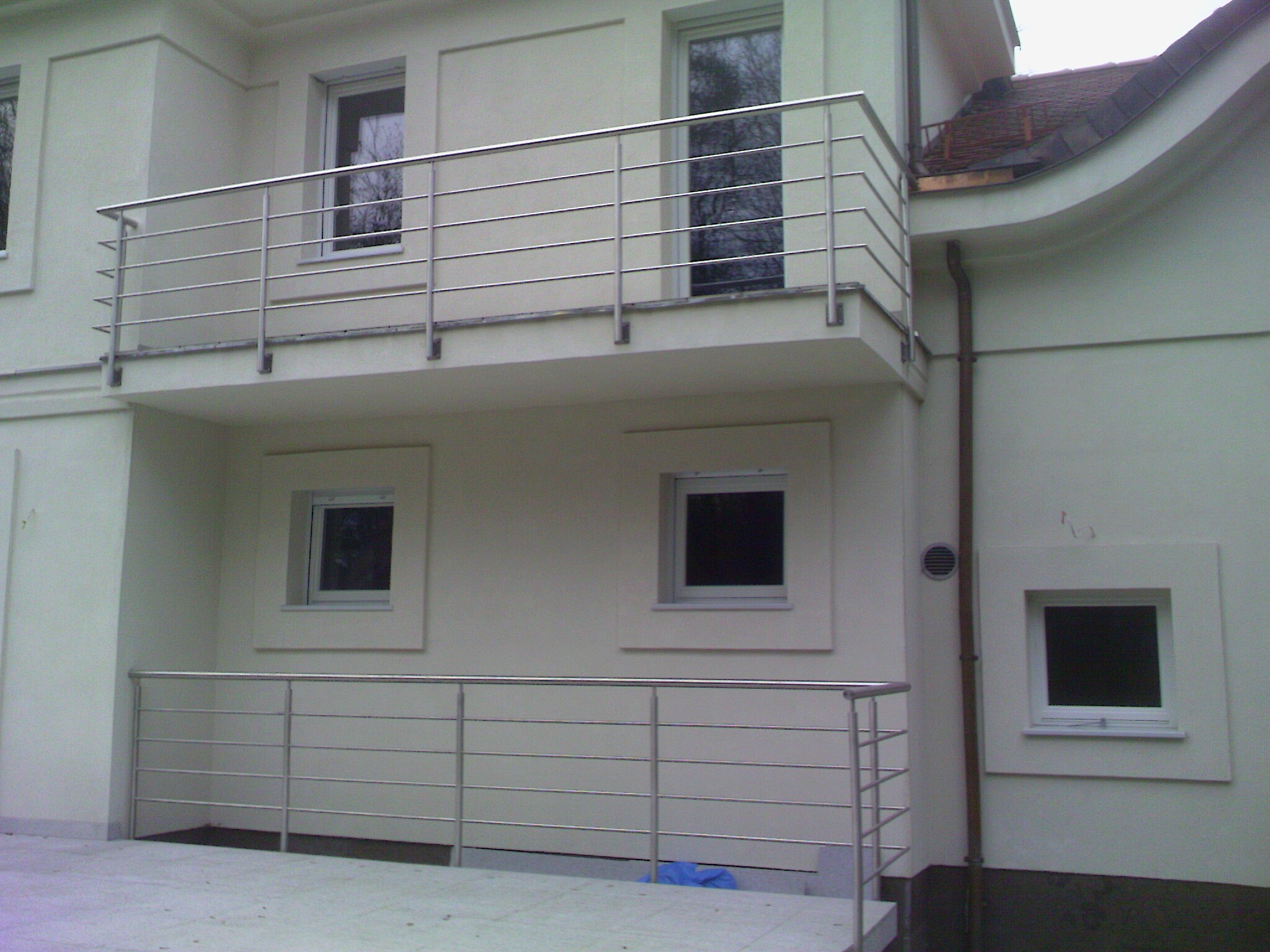 Zewnętrzny widok balkonu z prostą, poziomą balustradą ze stali nierdzewnej w Warszawie, z widocznymi elementami mocującymi do ściany budynku.