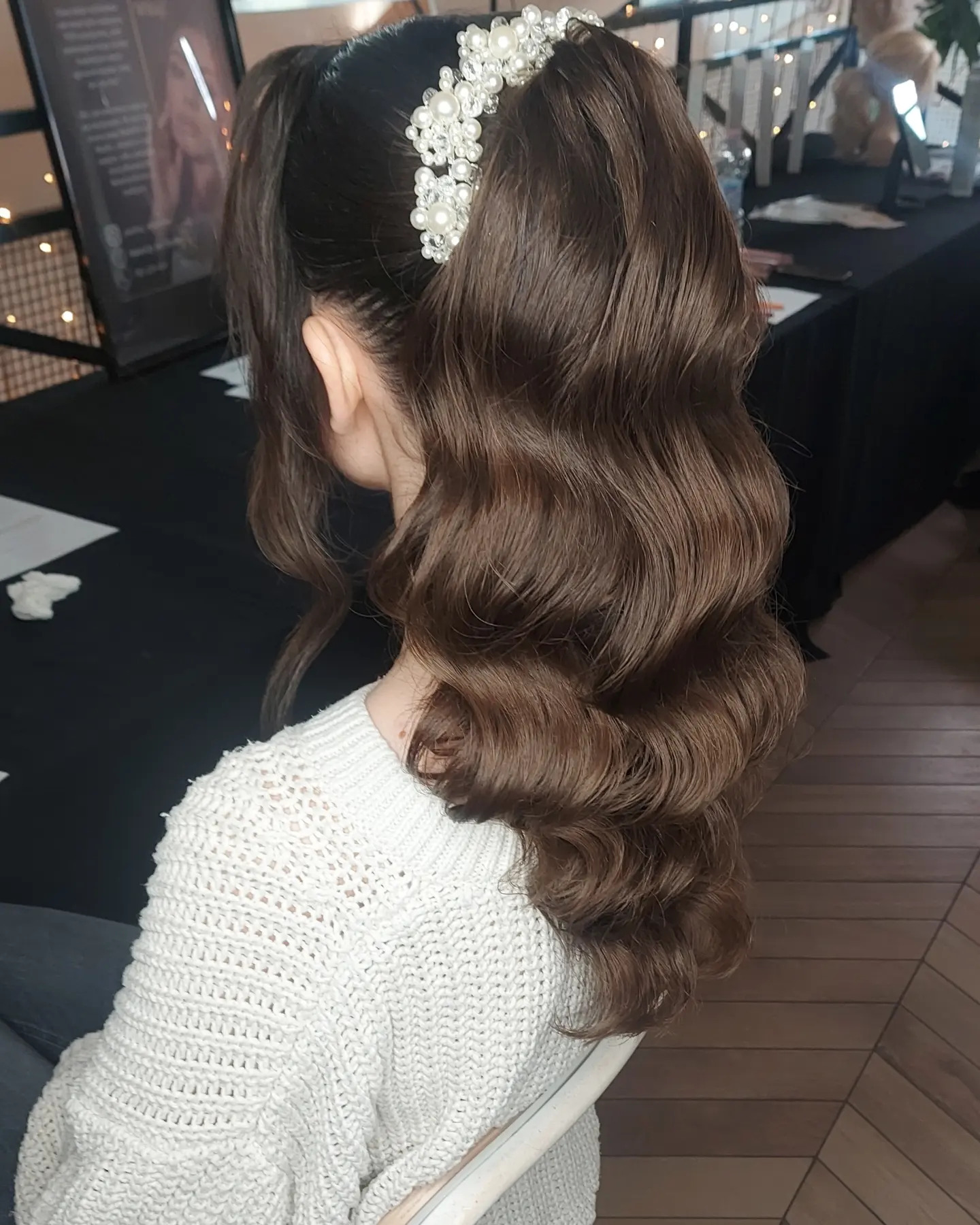 Elegancka fryzura z brązowych fal, upięta w koński ogon i ozdobiona perłową spinką, widok z tyłu. Subtelne oświetlenie podkreśla detale.