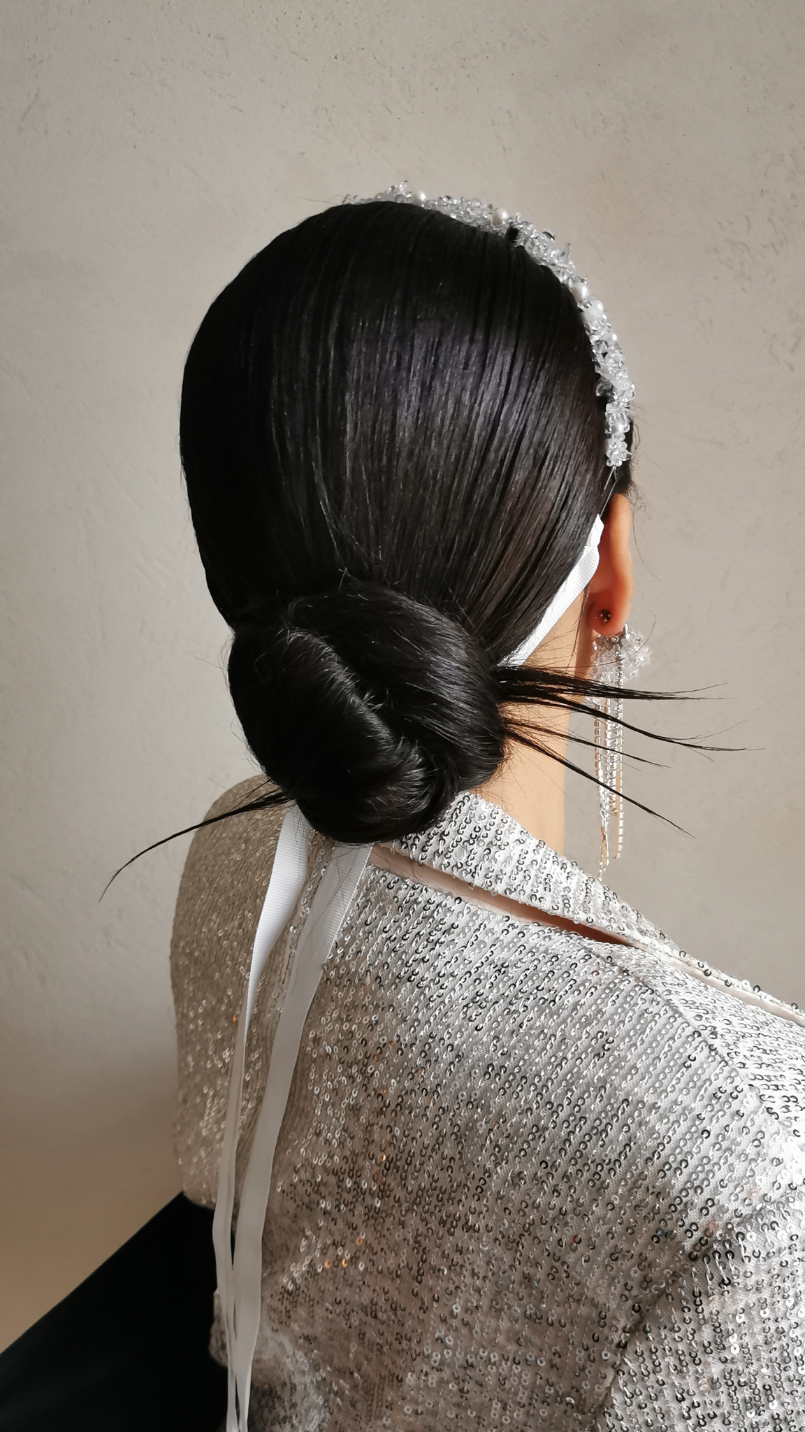 Elegancka fryzura upięta w kok, ozdobiona tiarą z kryształków i długimi kolczykami, widok z tyłu, błyszcząca kreacja.