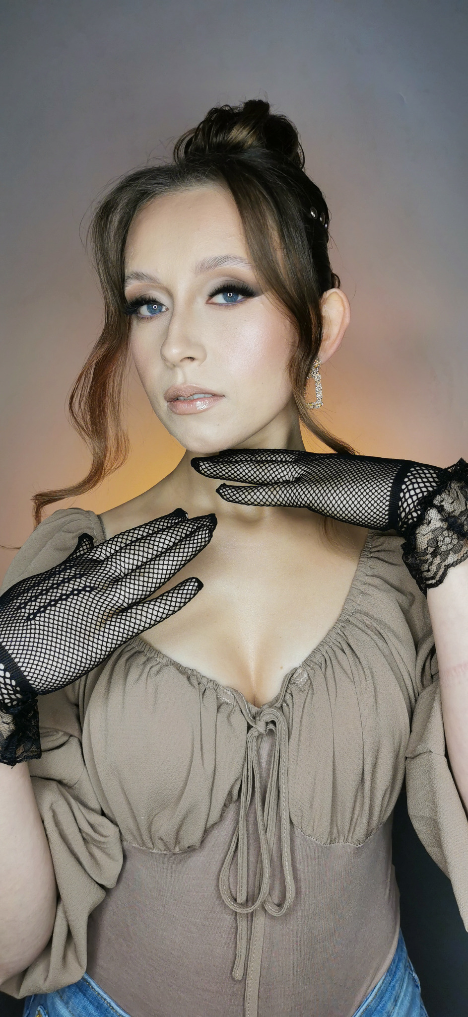 Portret kobiety z upiętymi włosami, w beżowej bluzce i czarnych rękawiczkach z siatki, prezentującej delikatny, profesjonalny make-up i biżuterię.