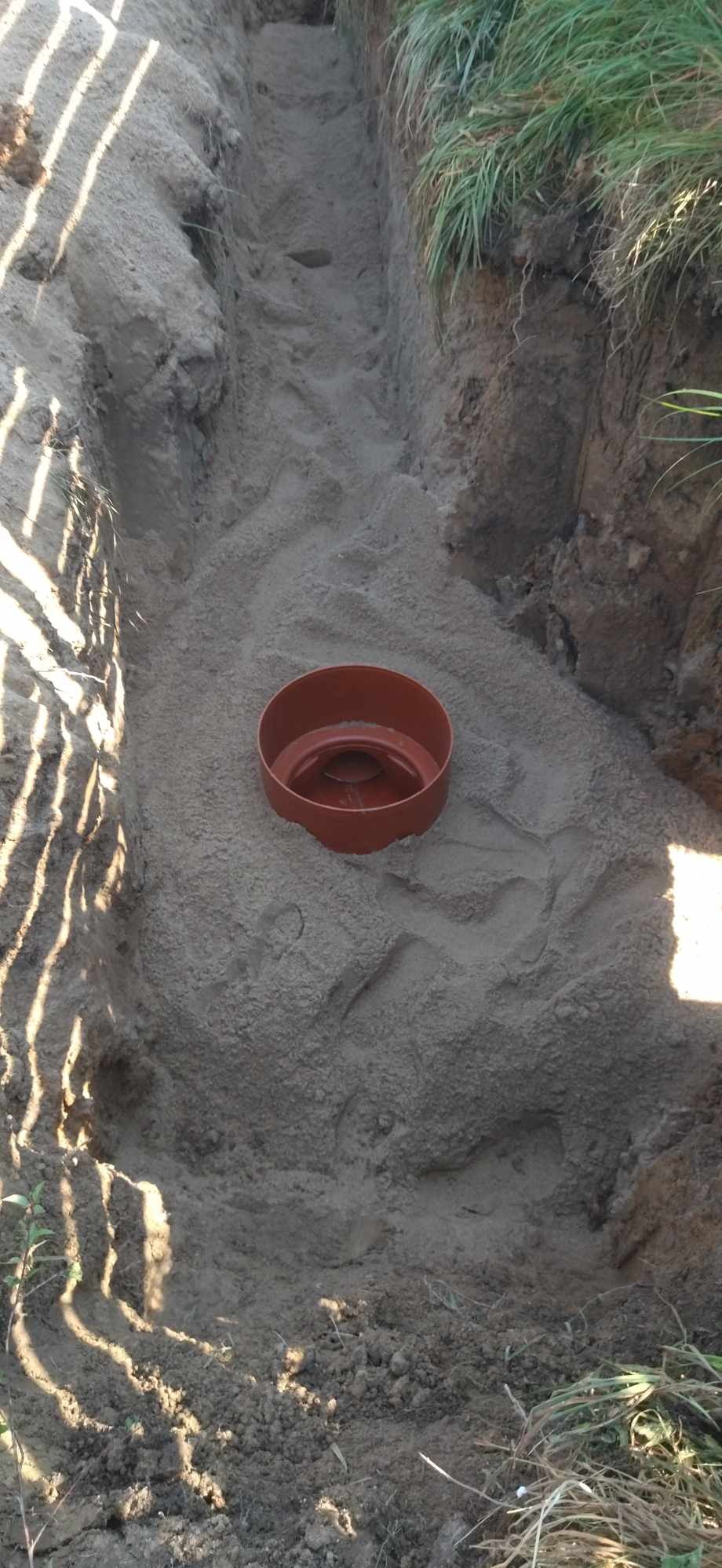 Wykonany wykop z piaskowym podsypem i wstawionym elementem betonowego szamba w trakcie montażu.