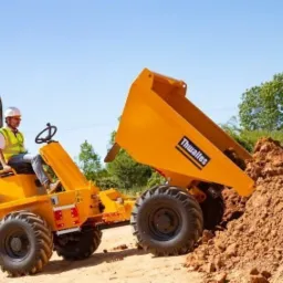 Żółta wywrotka Thwaites 3-tonowa wysypuje ziemię, operator w kasku i kamizelce odblaskowej, widok z boku na tle zieleni.