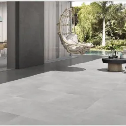 Ułożona szara, matowa, kwadratowa terakota na tarasie w Skomielnej Białej, widok na wiszący fotel, stoliki kawowe i basen w tle.
