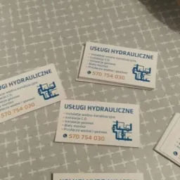 Kilka wizytówek firmy hydraulicznej z ofertą instalacji wodno-kanalizacyjnych, C.O., gazowych, białego montażu i przyłączy wodno-gazowych, leżących na wzorzystej powierzchni.