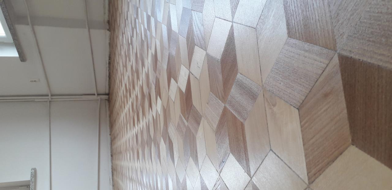 Ułożony parkiet w geometryczny wzór z jasnego i ciemnego drewna, widok z boku, ściana z grzejnikiem w tle.