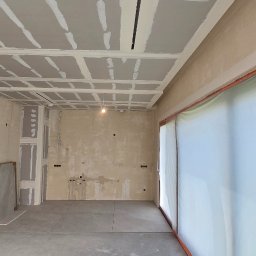 Tomasz Skoczylas - Wnętrze w trakcie prac wykończeniowych: sufit z płyt karton-gips, ściany przygotowane do malowania, widoczne instalacje elektryczne i sanitarne. Okno zabezpieczone folią.